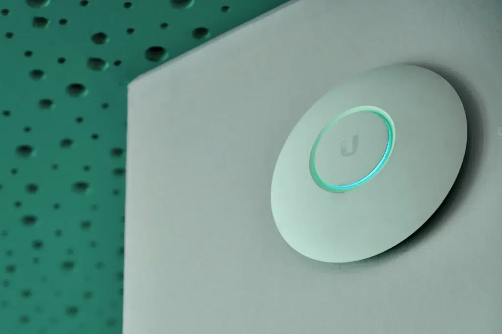 Uma imagem mostra um Access Point instalado em uma parede de um prédio comercial, proporcionando cobertura Wi-Fi em toda a área