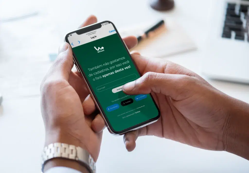 Imagem de uma mão segurando um smartphone com tela verde do aplicativo de login onde é informada a opção de cadastro temporário.