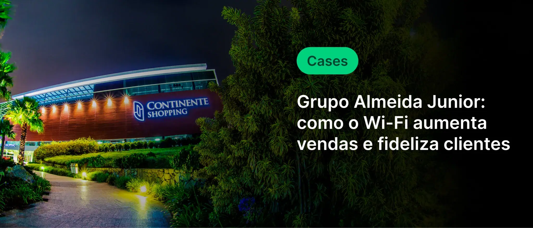 Imagem noturna de um shopping center com destaque para a fachada iluminada do Continente Shopping, ao lado de uma área com árvores e iluminação suave.