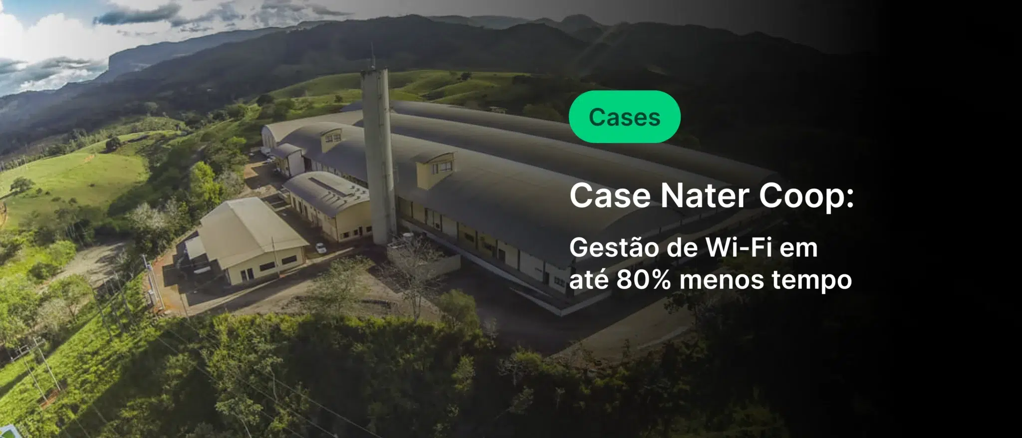 Imagem aérea da Case Nater Coop, uma fábrica inovadora que utiliza tecnologia de gestão de Wi-Fi para reduzir o consumo de energia em até 80%, localizada em uma área verde com montanhas ao fundo.