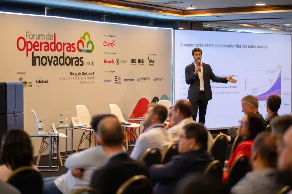Homem apresentando palestra em evento corporativo em sala de conferências, com plateia sentada e telões ao fundo mostrando o “Fórum de Operadoras Inovadoras” da Claro e dados sobre crescimento em redes móveis.